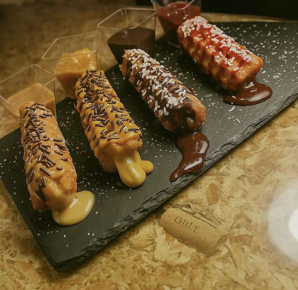 Cuatro churros D'Andux servidos sobre pizarra: chocolate intenso, dulce de leche, vainilla con coco y frambuesa
